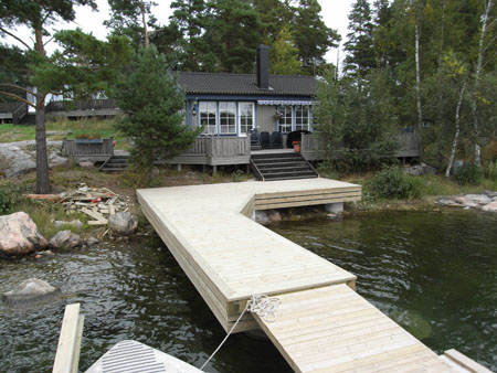 En vinklad träbrygga som följer strandkanten framför huset.